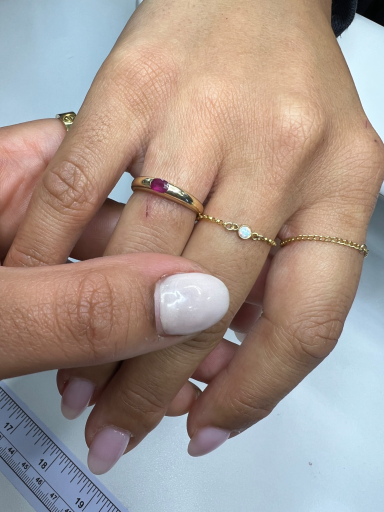 A hand with a gold ring and bracelet, featuring a pink gem and a small white stone.