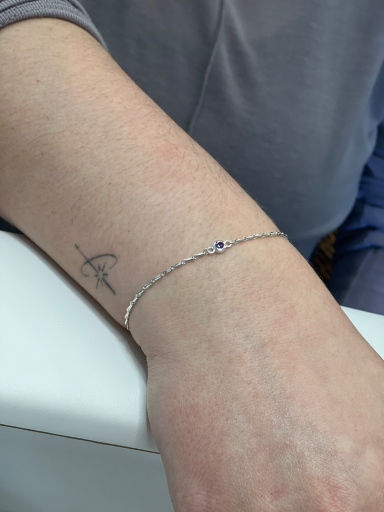 A silver bracelet with a small purple stone on a person's wrist.